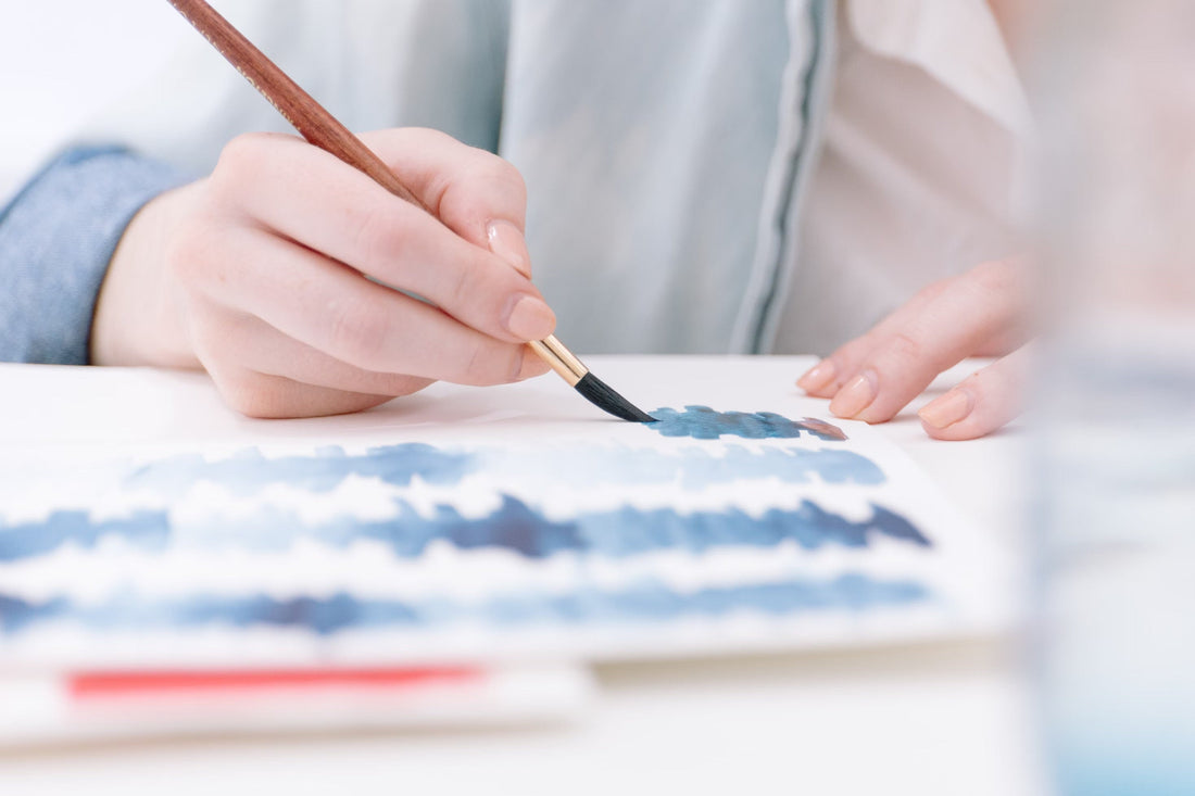 Close-up view of a person painting blue wavy lines with watercolor paint.